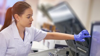 Photograph of a woman wearing a lab coat and rubber gloves who operates a computer application for medical diagnostics.